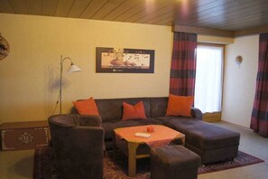Ein Wohnzimmer mit einer Couch, Sesseln, einem kleinen Tisch und einer Lampe.