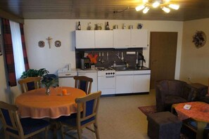 A compact kitchen with white cabinets, a stove, and a dining area with a table and chairs. - Holiday apartment in Böbrach with parking (Böbrach)