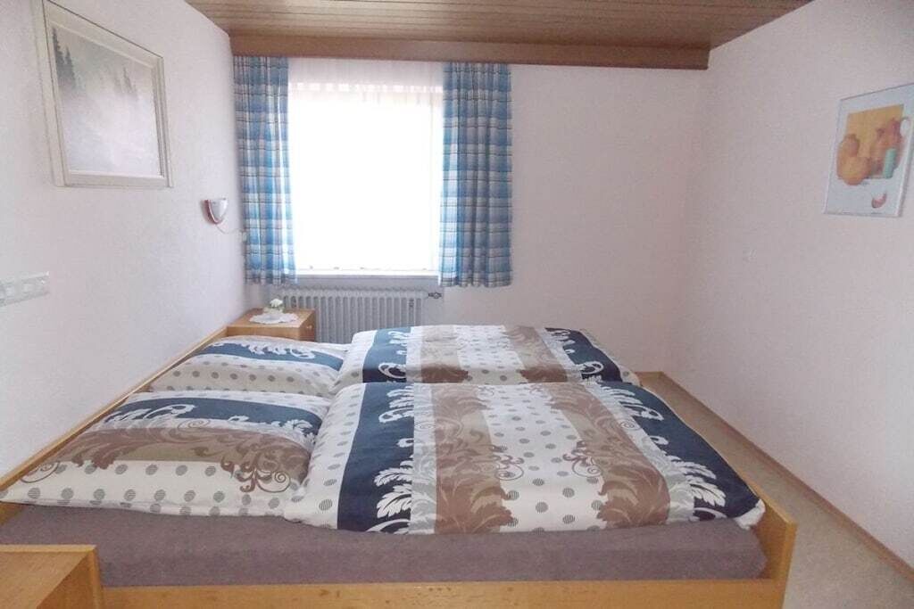 Una cama individual con colcha y almohadas estampadas, una mesita de noche, una ventana con cortinas y un radiador.
