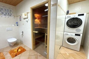 Een badkamer met toilet, een wasmachine en een sauna.