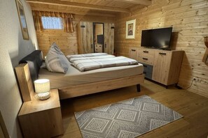 Een kamer met houten lambrisering, een bed, nachtkastje, televisie, kledingkast en een kamerbreed tapijt met dessin.