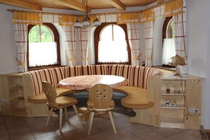 Een kamer met een ronde tafel, twee stoelen, een bankje en een kast met planken.