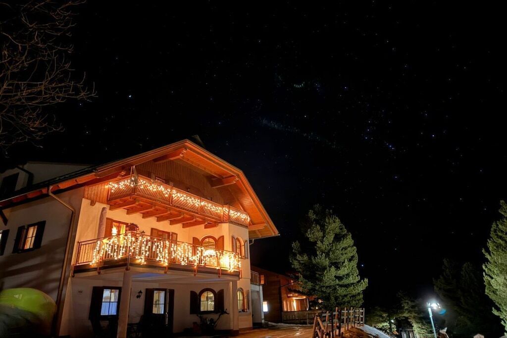 A two-story building with a balcony adorned with lights, surrounded by trees.