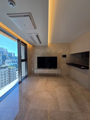A modern living room with a large flat-screen TV, a sliding glass door leading to a balcony, and a city view. - A brand-new, luxury high-end officetel in Seocho-dong (Seoul)