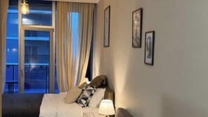 A modern living room with a sofa, a bed, and a balcony with curtains. - Komunna luxe (Batumi)