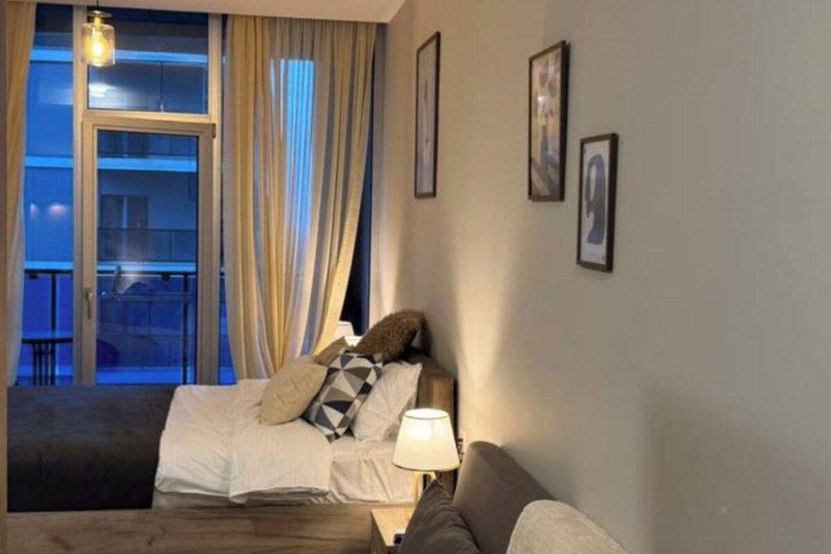 Ein modernes Wohnzimmer mit einer Couch, einem Bett und einem Balkon mit Vorhängen.