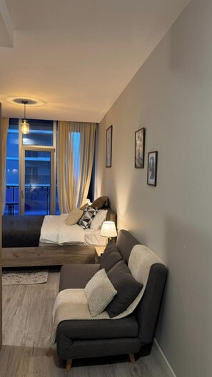 Ein modernes Wohnzimmer mit einer Couch, einem Bett und einem Balkon mit Vorhängen.