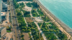 An aerial view of a coastal urban area with a beachfront promenade, buildings, and a parking lot. - Komunna luxe (Batumi)