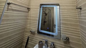 A bathroom with a shower, a sink with two basins, and a mirror with a light. - Komunna luxe (Batumi)