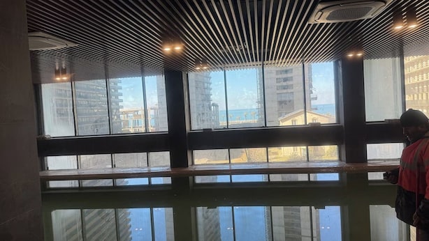 A modern interior with large windows, a reflective floor, and a person standing by the windows. - Komunna luxe (Batumi)
