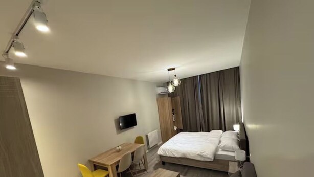A modern hotel room with a bed, a desk, a chair, a sofa, and a television. - Komunna luxe (Batumi)