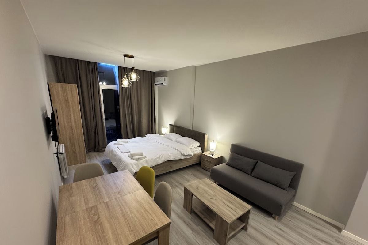 Ein modernes Hotelzimmer mit Bett, Sofa, Esstisch und einer kleinen Küchenzeile.
