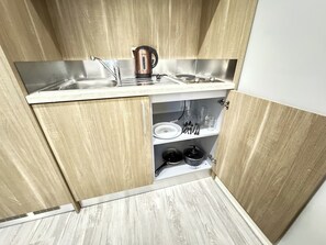 Una cocina compacta con un lavamanos de acero inoxidable, un hervidor y una estufa.