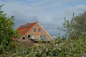 Een herenhuis met twee verdiepingen, een schuin dak, een zichtbare zolder en een klein houten bijgebouw.