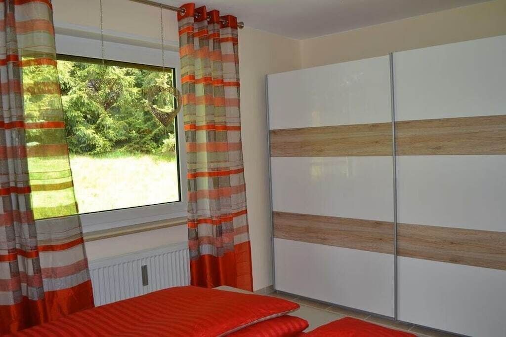 Een slaapkamer met raam, gordijnen, een bed en een kledingkast.