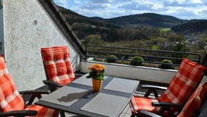 Un balcón con mesa y sillas, una planta en maceta y vistas a un valle.