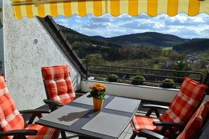 Un balcon avec une table et des chaises, un pot de fleurs et une vue sur une vallée.