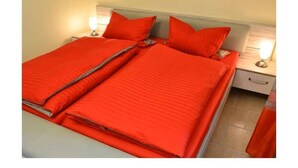 Una cama doble con ropa de cama roja y dos lámparas de noche.