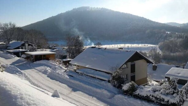 Un barrio residencial con casas cubiertas de nieve, cielo despejado y una montaña al fondo.