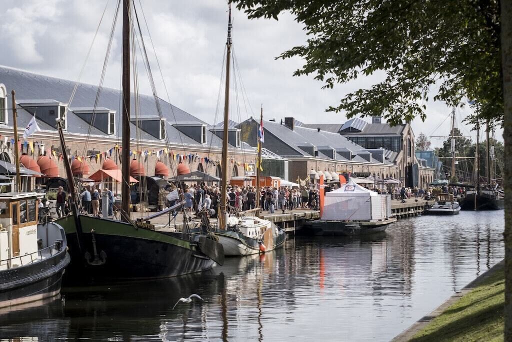 Un port de plaisance avec des bateaux amarrés, une foule de personnes et des bâtiments aux toits inclinés.