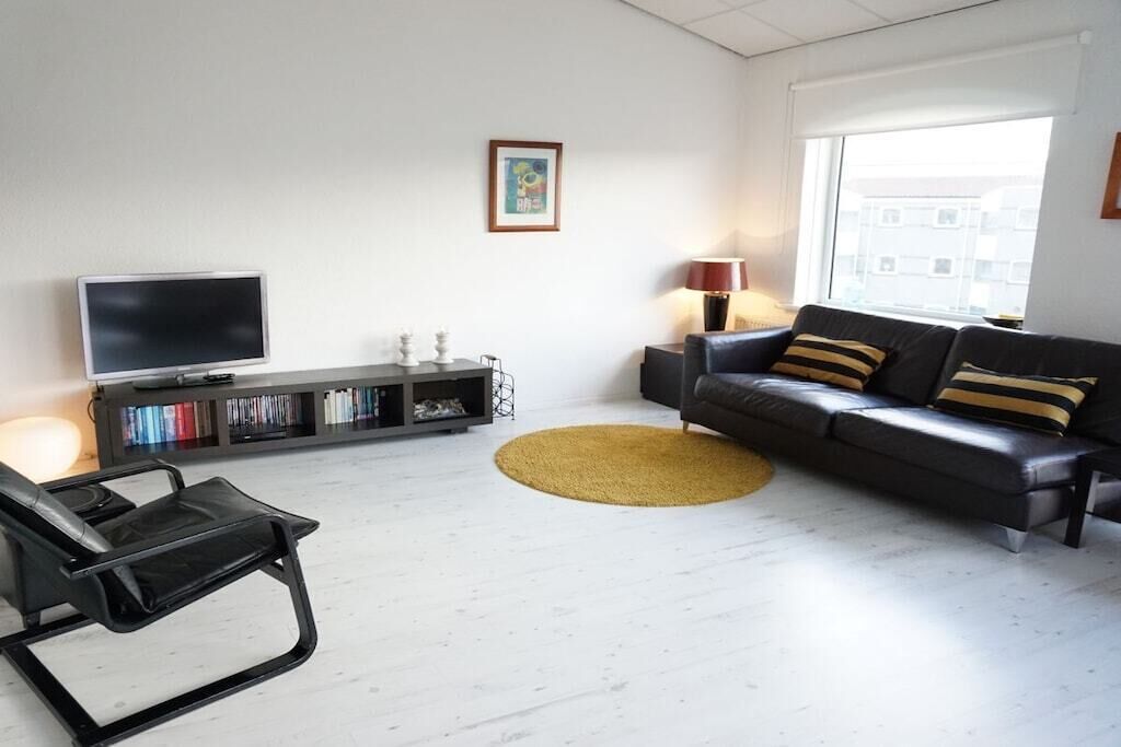 Un salon moderne avec un canapé, un téléviseur à écran plat, une bibliothèque et une fenêtre donnant sur un beau paysage.