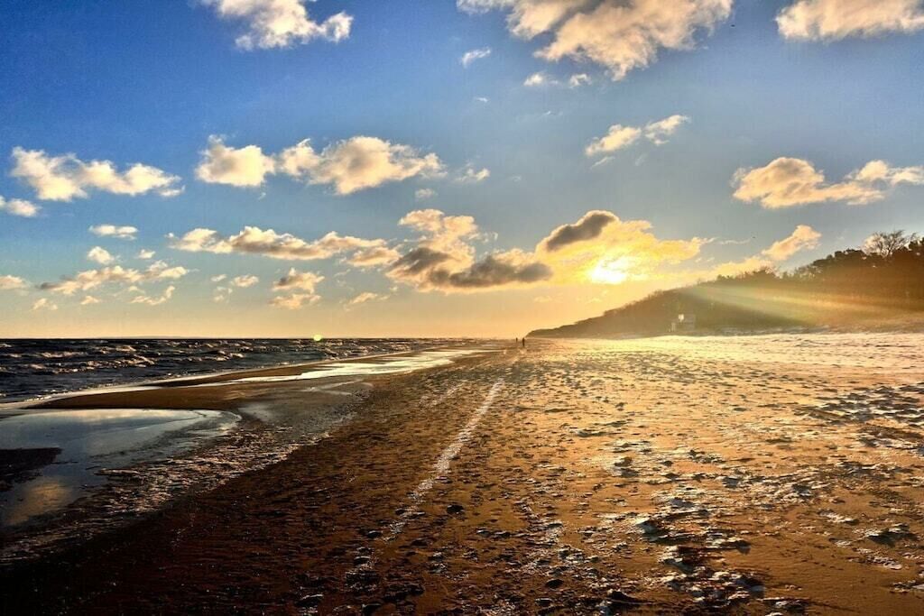Ein Strand mit blauem Himmel und Sonnenlicht, das im feuchten Sand glitzert.