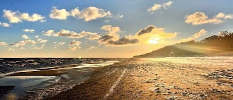 En strand med en klar himmel och solljus som reflekteras i den våta sanden.