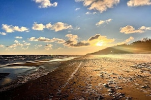 Uma praia com céu limpo e luz do sol refletindo na areia molhada.