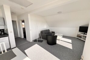 A modern apartment with a kitchenette, a gray sofa, a black coffee table, and a TV on a white stand. - Holiday apartment with 1 bedroom (Ückeritz)