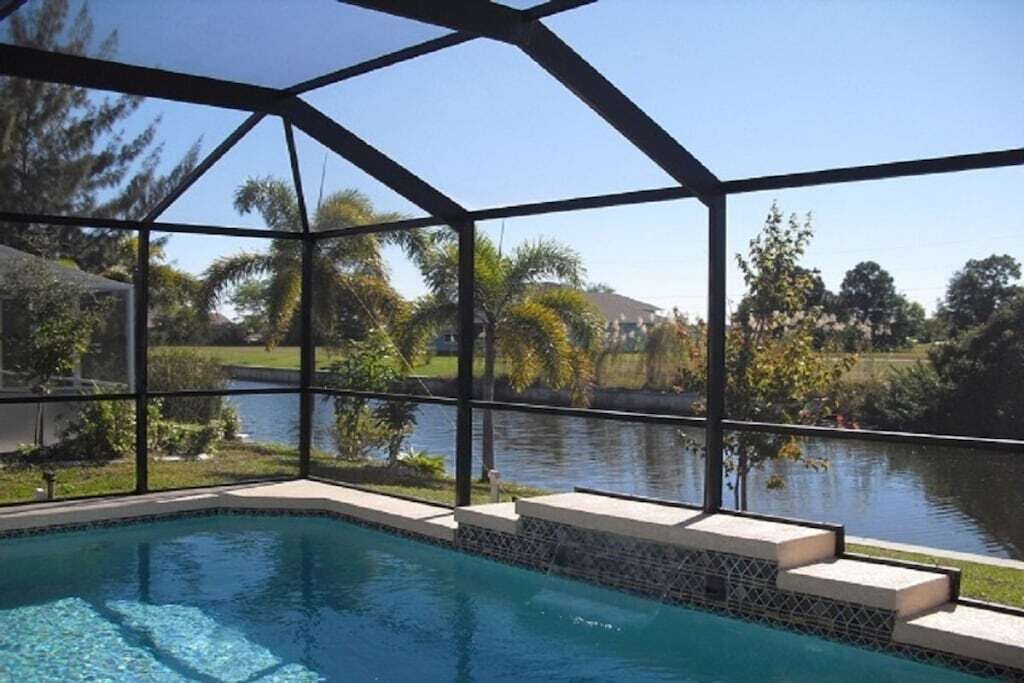 Une piscine dotée d’une structure en verre, entourée d’un jardin aménagé et bordée d’un plan d’eau.