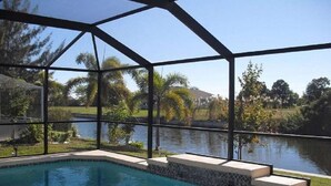 Piscina com estrutura de vidro, rodeada por um jardim ajardinado e um corpo d'água.