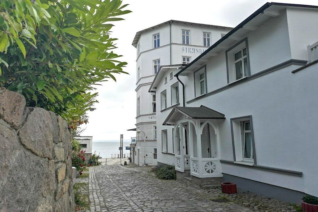 A white building with a stone wall and a cobblestone path leading to the sea.