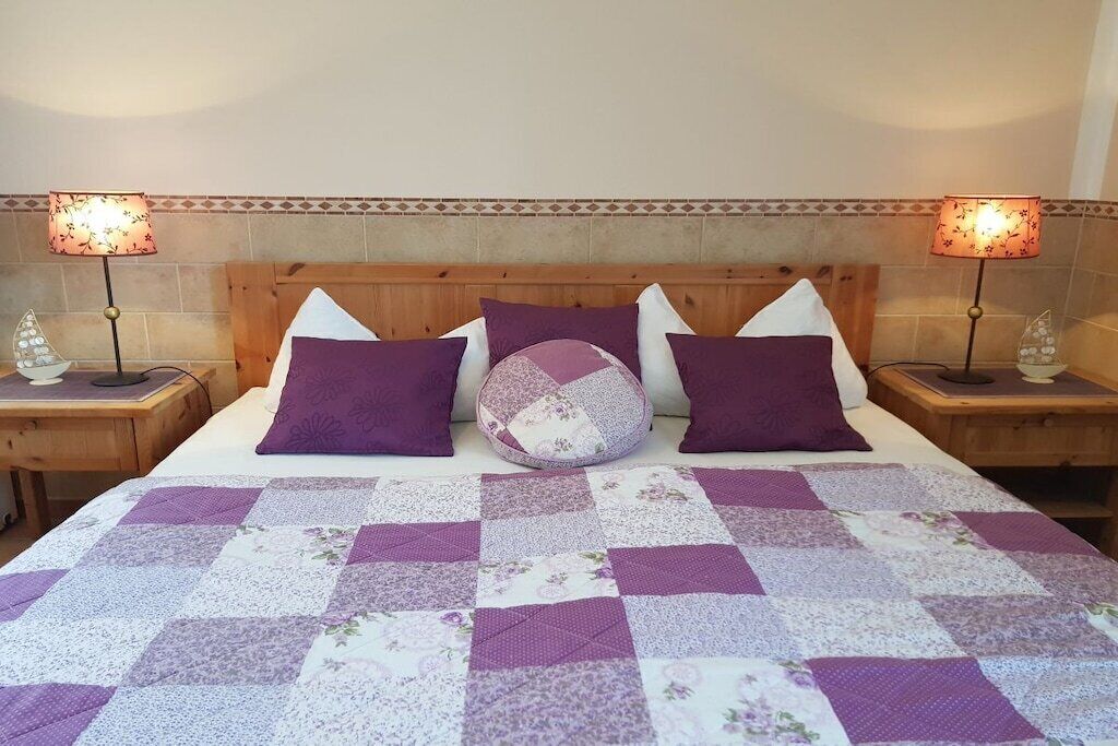 A bed with a purple and white quilt, flanked by two nightstands with lamps, and a wooden headboard.