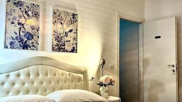 A bedroom with a tufted headboard, a bed with white linens, a bedside table with a vase, and a wardrobe.