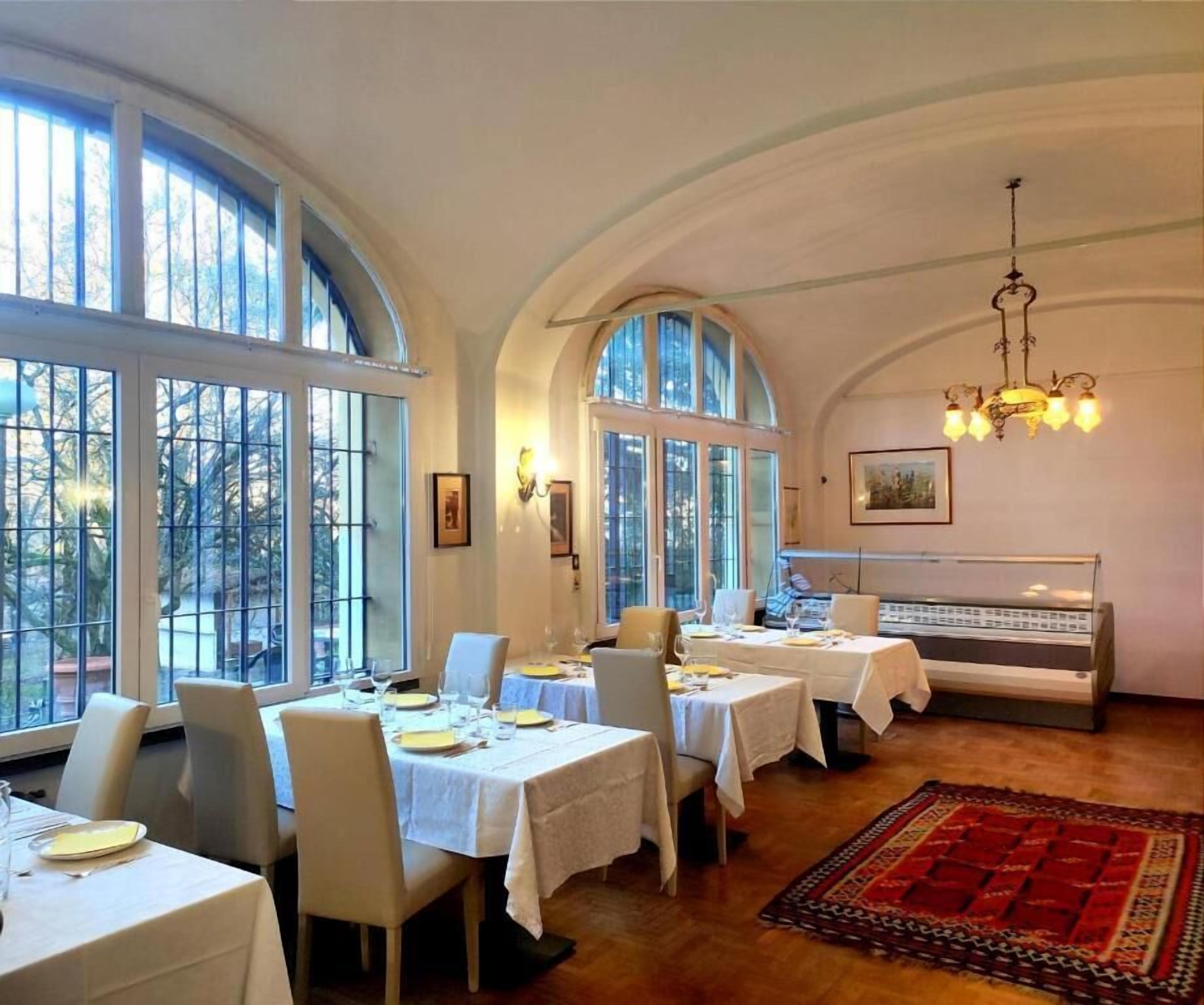 A dining area with tables set for a meal, large windows, and a piano in the background.
