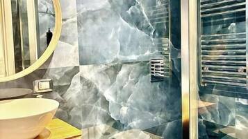 A bathroom with a marble wall, a round mirror, a sink, a bidet, and a toilet.