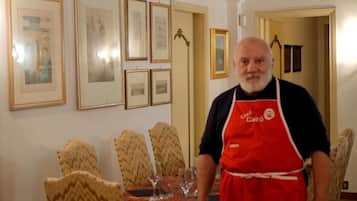 Zona pranzo con tavolo apparecchiato per quattro persone, quadri alle pareti e una persona in piedi sulla soglia.