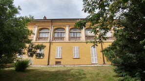 Un immeuble de deux étages avec une façade jaune, des fenêtres en arc de cercle et un balcon agrémenté d’une balustrade.