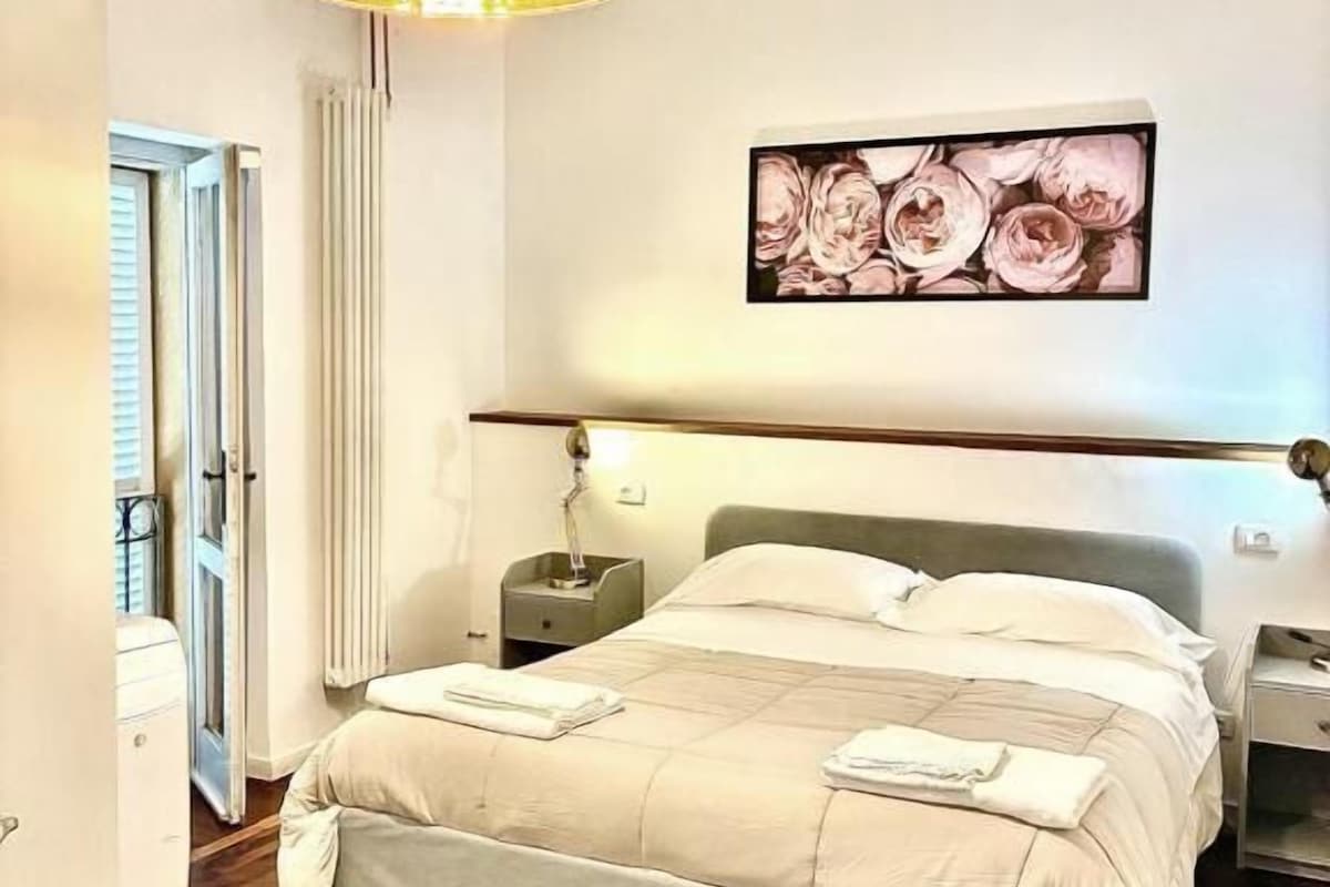 Une chambre à coucher avec un lit, des tables de chevet, une lampe, un tableau au mur et une porte.