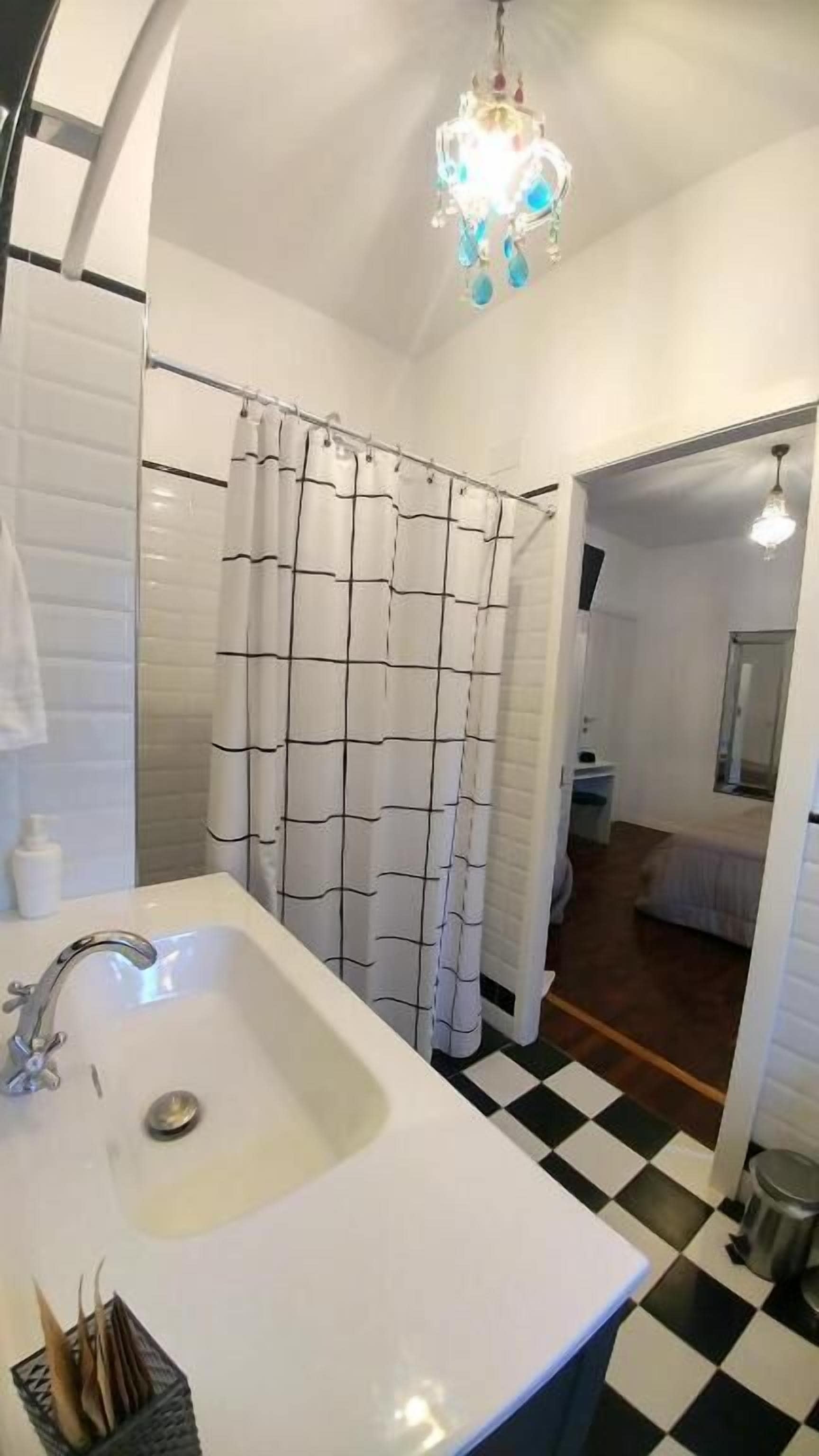 Un bagno con un lavandino bianco, una tenda da doccia e un lampadario.