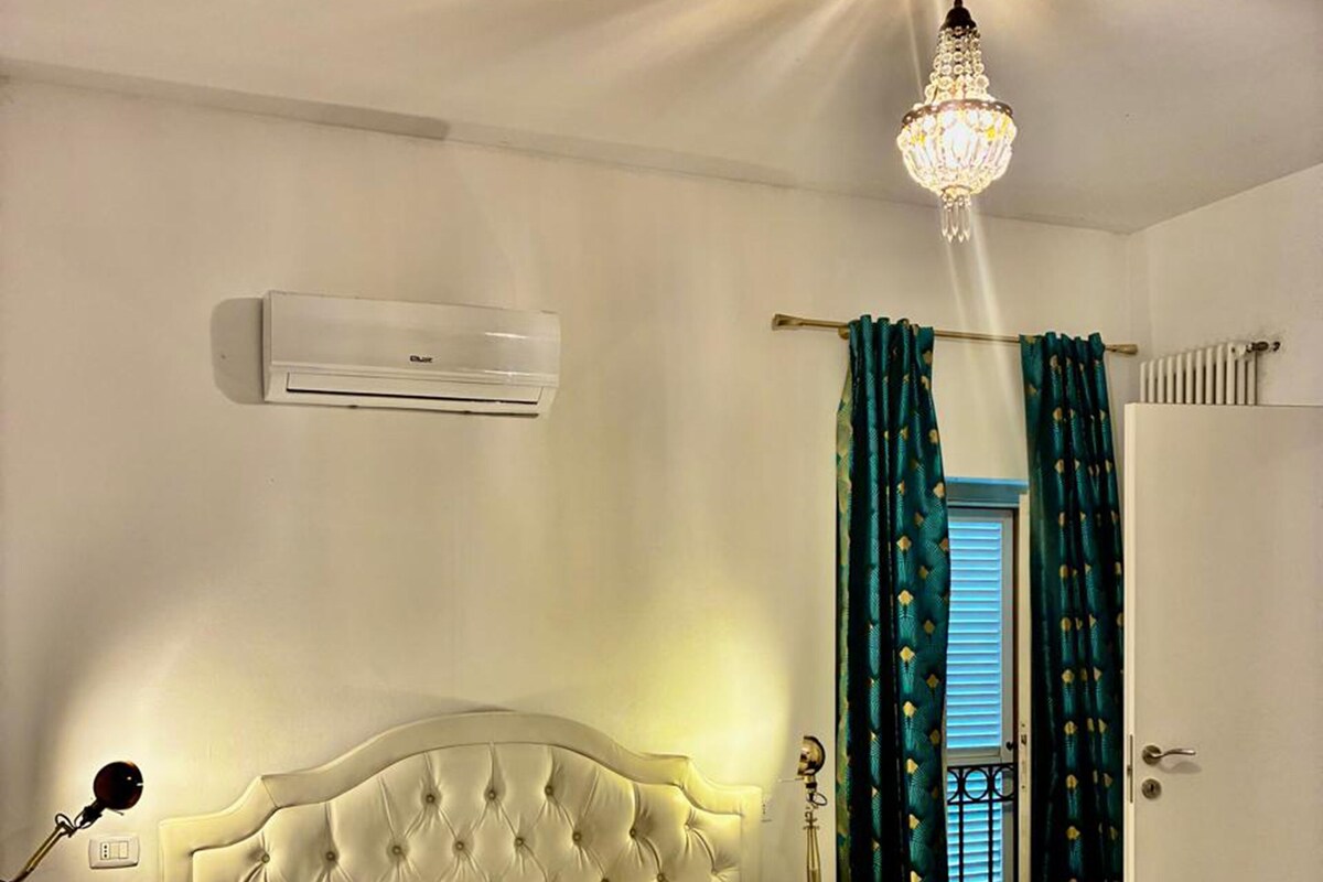 Un lit bien fait, avec une tête de lit, une lampe de chevet, un appareil de climatisation et une fenêtre avec des rideaux.