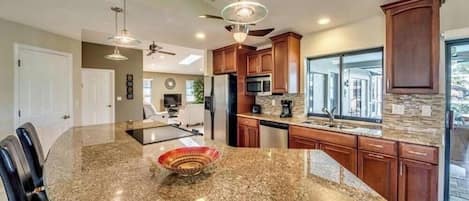 A kitchen with granite countertops, wooden cabinets, a large island, and pendant lighting.