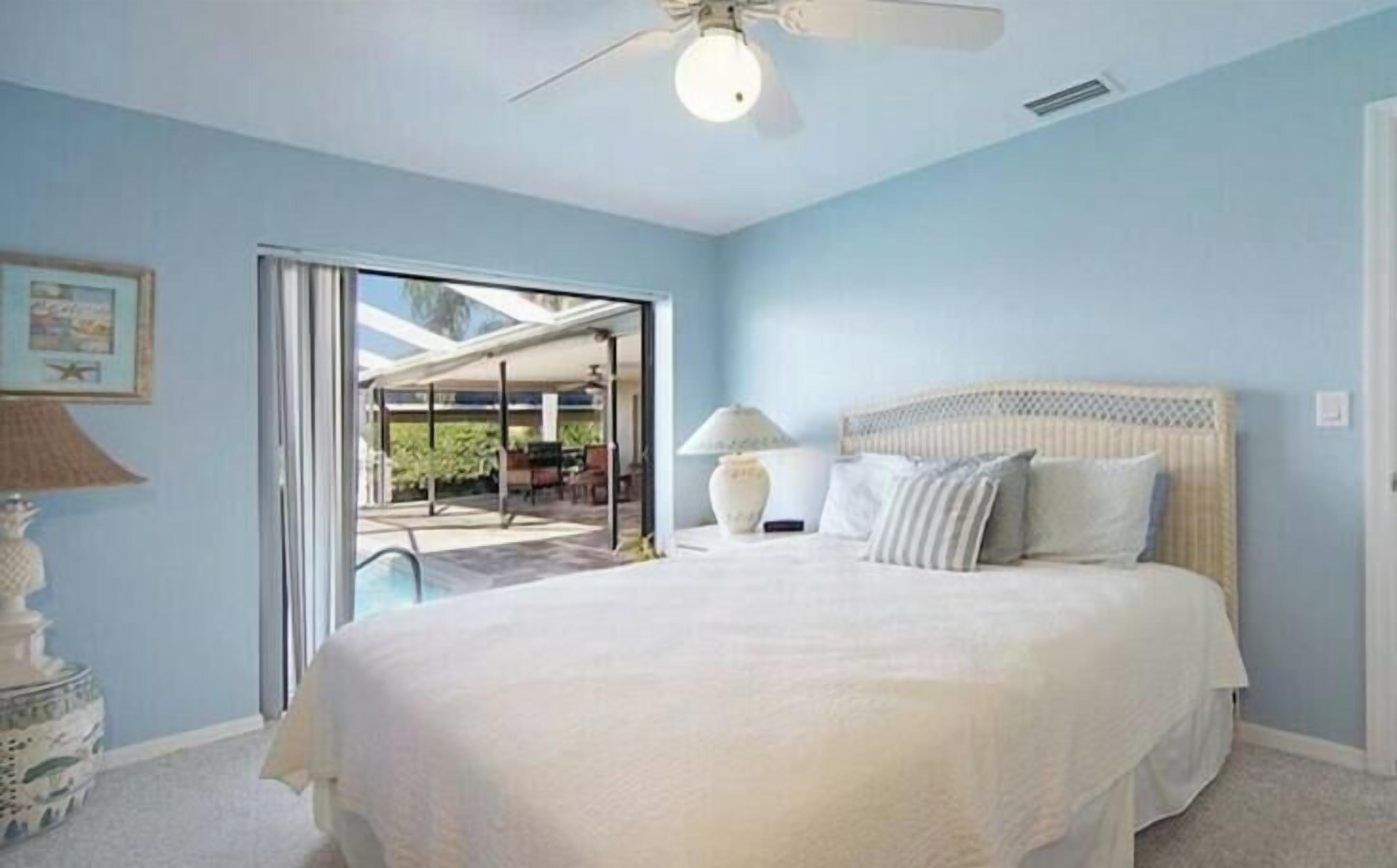 Une chambre avec un lit, un ventilateur de plafond et une vue sur un espace extérieur.