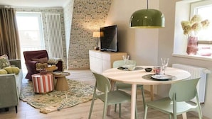 Un salon moderne avec une table à manger ronde, des chaises vertes, un téléviseur posé sur un meuble et un tapis à motifs.