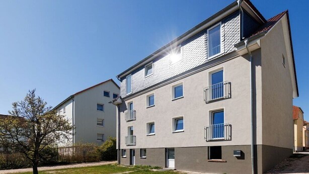 Un immeuble résidentiel à plusieurs étages, doté de balcons, avec un ciel dégagé et une pelouse bien entretenue.