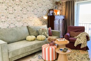 Ein Wohnzimmer mit einer Couch, einem Sessel, einem kleinen Tisch mit Schachfiguren und einem Schrank.