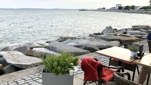 Un restaurant en bord de mer avec une terrasse, une vue sur la mer et un mur en pierre.