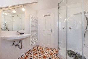 Een badkamer met een douchecabine van glas, een witte wastafel en een vloer met een patroon.