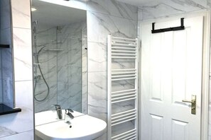 Een badkamer met een douchecabine van glas, een witte wastafel en een handdoekhouder.