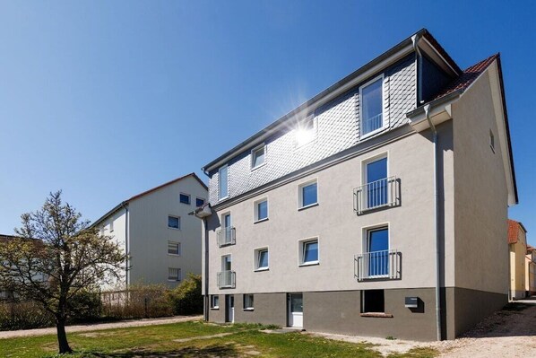 Een meerlaags woongebouw met balkons, een heldere lucht en een verzorgd gazon.